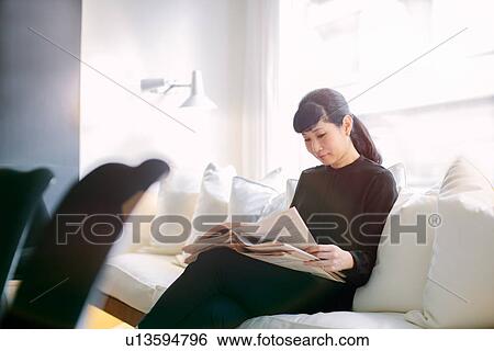 Stock Photograph - Mature businesswoman reading newspaper on boardroom sofa. Fotosearch