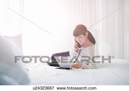 Mature businesswoman reading notes whilst talking on hotel room telephone View Large Photo Image Stock Photo - Mature businesswoman reading notes whilst talking on hotel room telephone. Fotosearch