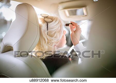 Stock Photo - "Mature businesswoman sitting in car, applying make-up, rear view". Fotosearch