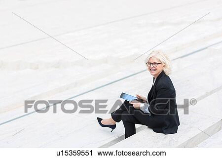 "Mature businesswoman sitting on wall, smiling, holding digital tablet" View Large Photo Image Stock Image - "Mature businesswoman sitting on wall, smiling, holding digital tablet". Fotosearch