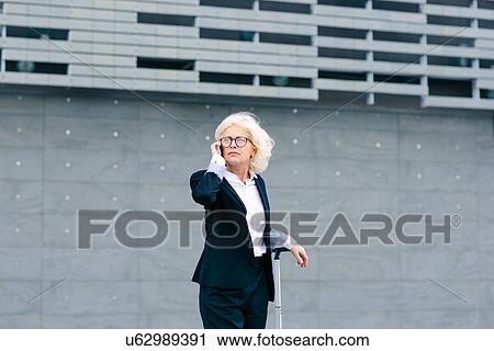 "Mature businesswoman standing with suitcase, using mobile phone" View Large Photo Image Stock Image - "Mature businesswoman standing with suitcase, using mobile phone". Fotosearch