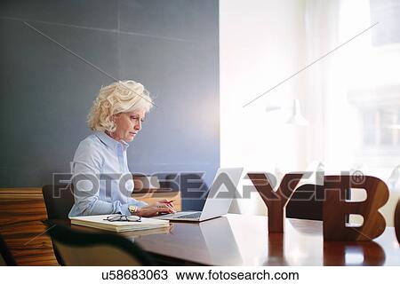 Mature businesswoman using laptop at boardroom table View Large Photo Image Stock Image - Mature businesswoman using laptop at boardroom table. Fotosearch
