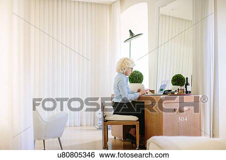 Mature businesswoman using laptop at hotel room desk View Large Photo Image Stock Photograph - Mature businesswoman using laptop at hotel room desk. Fotosearch