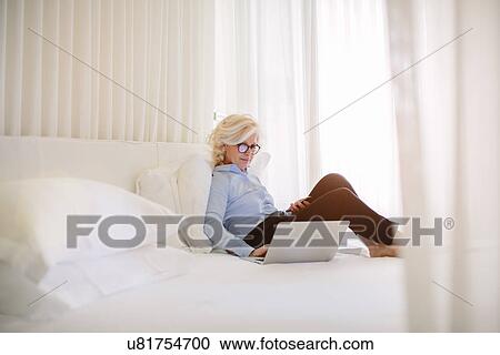 Mature businesswoman using laptop on hotel room bed View Large Photo Image Stock Image - Mature businesswoman using laptop on hotel room bed. Fotosearch