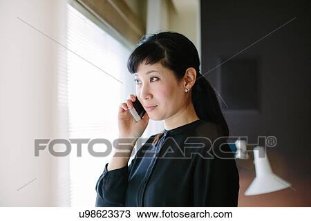 Mature businesswoman using smartphone whist looking out of hotel room window View Large Photo Image Stock Image - Mature businesswoman using smartphone whist looking out of hotel room window. Fotosearch
