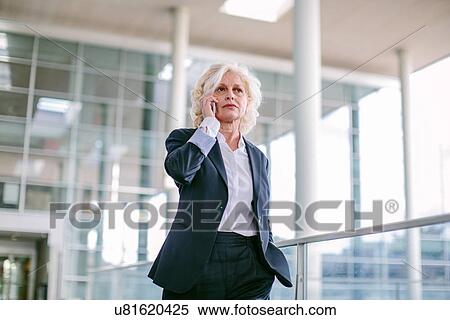 "Mature businesswoman walking along walkway, using mobile phone, low angle view" View Large Photo Image Stock Photography - "Mature businesswoman walking along walkway, using mobile phone, low angle view". Fotosearch