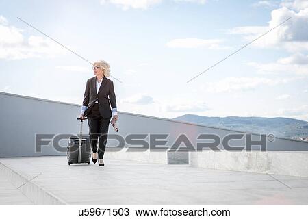 Mature businesswoman walking with suitcase View Large Photo Image Stock Image - Mature businesswoman walking with suitcase. Fotosearch
