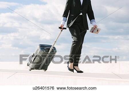 Stock Photograph - "Mature businesswoman walking with suitcase, low section". Fotosearch