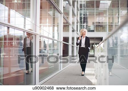"Mature businesswoman wearing earphones, walking along corridor" View Large Photo Image Stock Photo - "Mature businesswoman wearing earphones, walking along corridor". Fotosearch