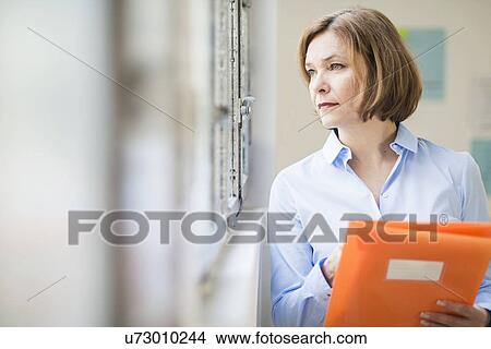 Mature businesswoman with file gazing out of office window View Large Photo Image Picture - Mature businesswoman with file gazing out of office window. Fotosearch