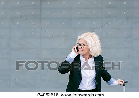 "Mature businesswoman with suitcase, using mobile phone" View Large Photo Image Stock Photograph - "Mature businesswoman with suitcase, using mobile phone". Fotosearch