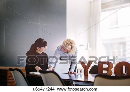 Mature businesswomen using laptop and chatting at boardroom table View Large Photo Image Picture - Mature businesswomen using laptop and chatting at boardroom table. Fotosearch