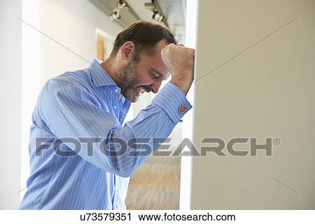 Stock Image - Mature man banging fist on wall in corridor. Fotosearch