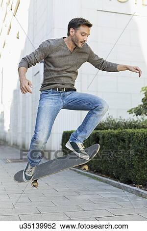 Stock Image - Mature man doing mid air skateboarding trick on sidewalk. Fotosearch