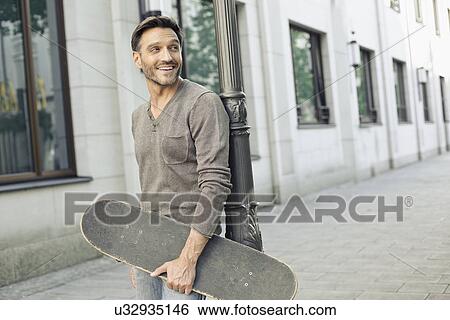 Mature man leaning against lamppost holding skateboard View Large Photo Image Stock Photograph - Mature man leaning against lamppost holding skateboard. Fotosearch