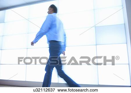 Stock Photo - Mature man walking past backlit wall panels. Fotosearch