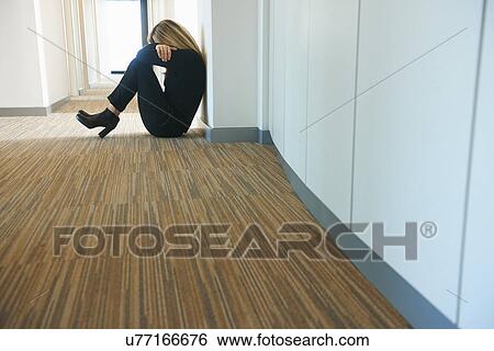 Stock Photograph - Mature woman sitting against wall in corridor. Fotosearch
