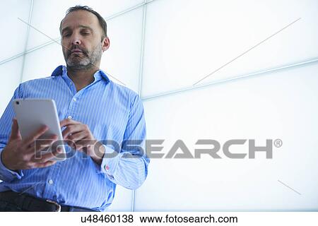Stock Photo - Mature woman using digital tablet backlit wall panels. Fotosearch