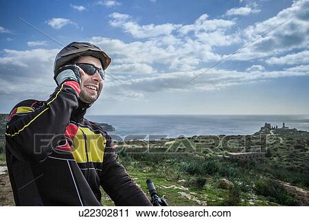 "Mid adult male mountain biker chatting on smartphone from coastal path, Cagliari, Sardinia, Italy" View Large Photo Image Stock Image - "Mid adult male mountain biker chatting on smartphone from coastal path, Cagliari, Sardinia, Italy". Fotosearch