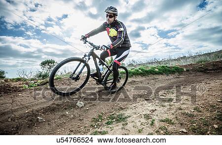 Picture - "Mid adult male mountain biker speeding on track corner, Cagliari, Sardinia, Italy". Fotosearch