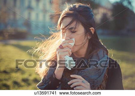 Stock Image - Mid adult woman blowing nose with handkerchief in park. Fotosearch