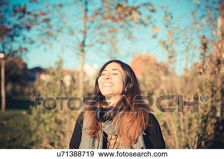 Stock Photo - Mid adult woman laughing with eyes closed in park. Fotosearch
