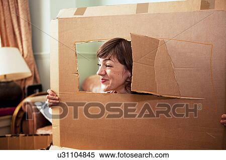 Mid adult woman peeking out of cardboard box window in living room View Large Photo Image Stock Photography - Mid adult woman peeking out of cardboard box window in living room. Fotosearch