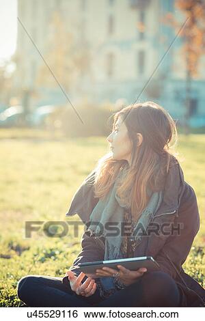 Mid adult woman sitting cross legged using digital tablet in park View Large Photo Image Stock Photograph - Mid adult woman sitting cross legged using digital tablet in park. Fotosearch
