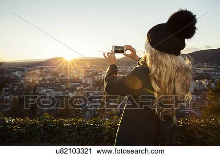 Stock Image - "Mid adult woman taking photo on phone, Graz, Styria, Austria". Fotosearch