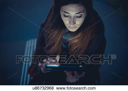 Stock Photo - Mid adult woman using digital tablet touchscreen on railway platform at dusk. Fotosearch