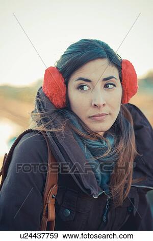 Stock Photo - Mid adult woman wearing red ear muffs in park. Fotosearch