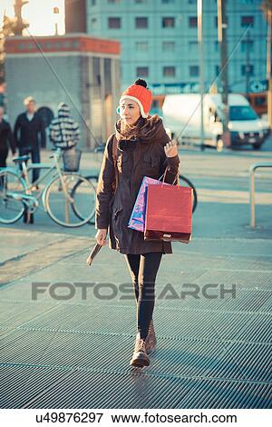 Stock Photo - Mid adult woman wearing red pom pom hat strolling with shopping bags. Fotosearch