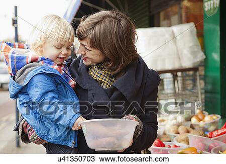 Stock Image - Mother and son shopping at street market stall. Fotosearch