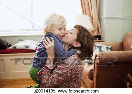 Stock Photography - Mother holding up and kissing son in living room. Fotosearch