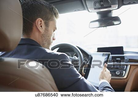 Stock Image - Over the shoulder view of young businessman using digital tablet in car. Fotosearch