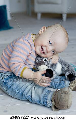 Portrait of baby girl sitting on living room floor hugging soft toy View Large Photo Image Stock Photo - Portrait of baby girl sitting on living room floor hugging soft toy. Fotosearch