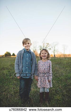 Stock Image - Portrait of boy holding sisters hand in field. Fotosearch