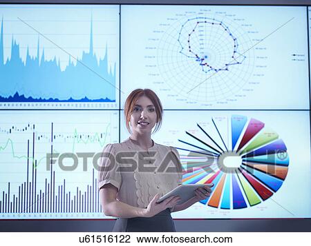 Stock Image - Portrait of businesswoman making presentation in front of graphs on screen. Fotosearch