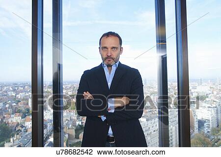 Stock Image - "Portrait of confident businessman in front of office window with Brussels cityscape, Belgium". Fotosearch