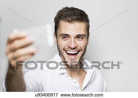 Portrait of laughing young man taking smartphone selfie View Large Photo Image Stock Photo - Portrait of laughing young man taking smartphone selfie. Fotosearch
