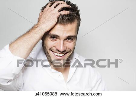 Stock Photo - Portrait of laughing young man with hand in hair. Fotosearch