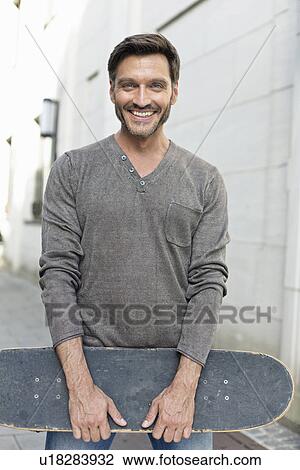 Portrait of mature man holding skateboard on sidewalk View Large Photo Image Stock Image - Portrait of mature man holding skateboard on sidewalk. Fotosearch