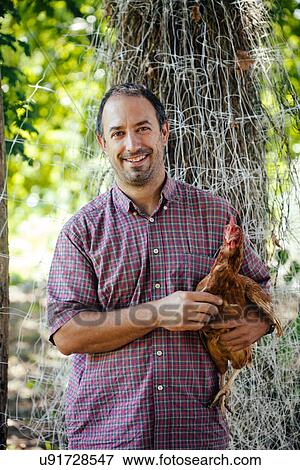 Stock Photo - "Portrait of mid adult man holding free range hen, Tuscany, Italy". Fotosearch