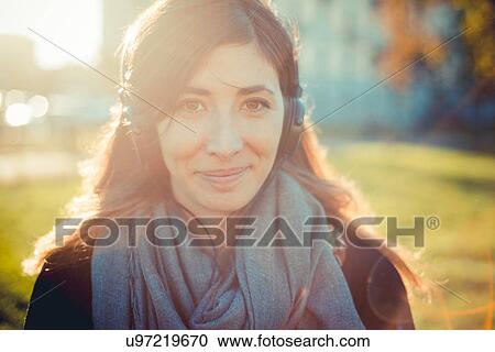 Portrait of mid adult woman listening to headphones in park View Large Photo Image Stock Image - Portrait of mid adult woman listening to headphones in park. Fotosearch
