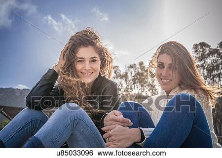 Portrait of two young women friends sitting on breezy beach View Large Photo Image Stock Photograph - Portrait of two young women friends sitting on breezy beach. Fotosearch