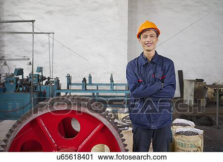 Stock Image - "Portrait of worker next to cog wheel in crane factory, Jiangsu Province, China". Fotosearch