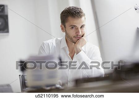 Portrait of young businessman with chin on hand at office desk View Large Photo Image Stock Photography - Portrait of young businessman with chin on hand at office desk. Fotosearch