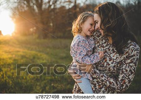 Portrait of young woman carrying daughter in field View Large Photo Image Stock Photo - Portrait of young woman carrying daughter in field. Fotosearch