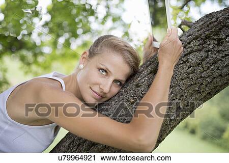 Portrait of young woman resting in tree holding digital tablet View Large Photo Image Stock Image - Portrait of young woman resting in tree holding digital tablet. Fotosearch