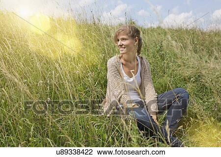 Stock Image - Portrait of young woman sitting in field. Fotosearch